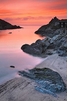 the sun is setting over the water and rocks