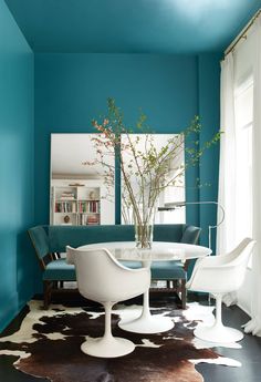 a dining room with blue walls and white chairs in the center, an oval table surrounded by tulips