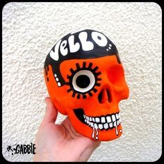 a hand holding an orange and black skull with the word hello painted on it's face