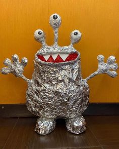 a tin foil monster sitting on top of a wooden floor next to a yellow wall