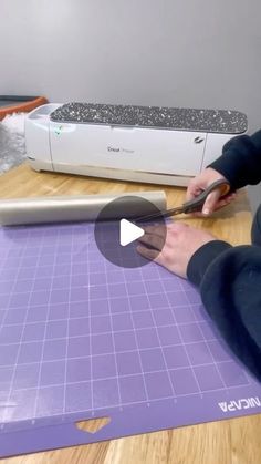 a person cutting paper on top of a wooden table with a machine in the background