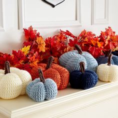 crocheted pumpkins sitting on a mantle with autumn leaves