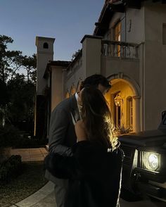 a man and woman standing in front of a house at night with the lights on