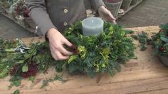 someone is making a wreath out of greenery and candlesticks on a wooden table