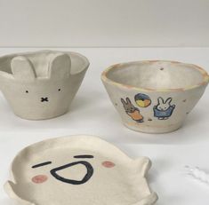 three ceramic bowls with faces on them, one has an animal face and the other has a rabbit's head