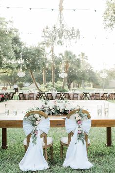 two chairs with bows and flowers on them are set up for an outdoor wedding reception