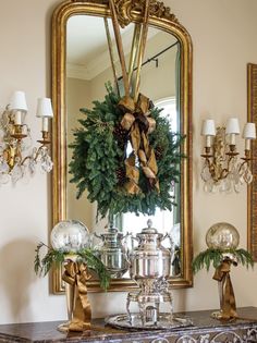 a christmas wreath on top of a table in front of a mirror and chandelier