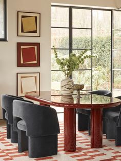 a dining room table surrounded by chairs in front of a large window with pictures on the wall