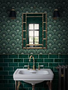 a white sink sitting under a mirror next to a green tiled wall with gold fixtures