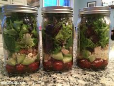 three mason jars filled with salads sitting on top of a counter