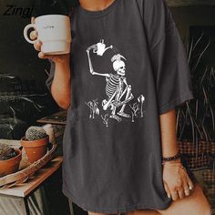 a woman holding a coffee cup in her right hand while wearing a skeleton t - shirt