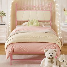 a pink bed with two teddy bears sitting on the floor in front of it,