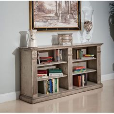 an old book shelf with books and vases on it in front of a painting