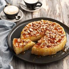 a cake on a plate with one slice cut out and topped with almonds next to a cup of coffee