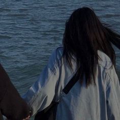 two people holding hands walking along the water