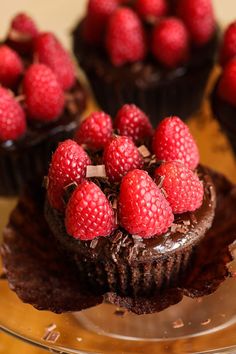 chocolate cupcakes topped with raspberries on a glass platter, ready to be eaten