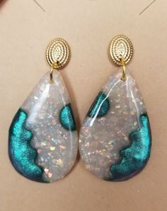 a pair of white and blue earrings on top of a piece of paper with gold accents