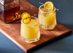 two glasses filled with drinks sitting on top of a wooden cutting board