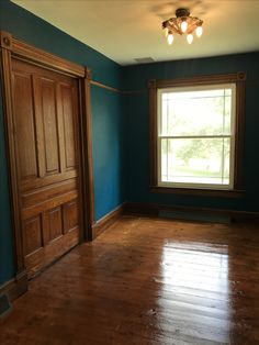 an empty room with blue walls and wood floors, two doors open to the other side