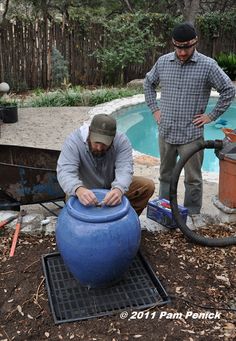 two men are working on something in the ground next to a pool with a large blue pot