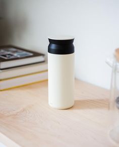 a white and black cup sitting on top of a wooden table next to a stack of books