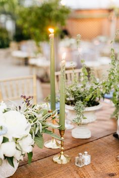 a wooden table topped with white flowers and greenery next to tall candlesticks