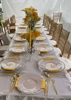 the table is set with yellow and white plates, silverware, and flowers in vases