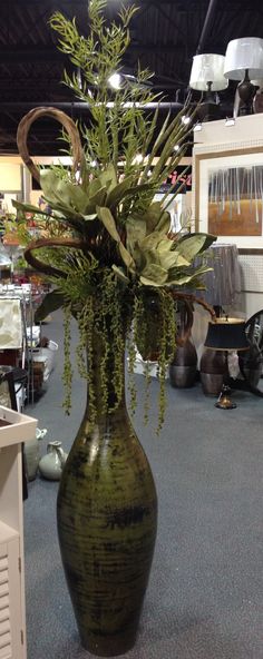 a green vase filled with lots of greenery on top of a blue carpeted floor