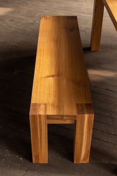 a wooden bench sitting on top of a floor next to a table with two legs