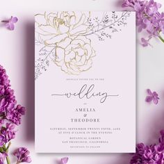 the wedding card is surrounded by purple flowers and greenery, with gold foil lettering