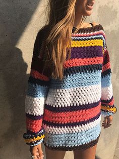 a woman standing in front of a wall wearing a multicolored crochet sweater