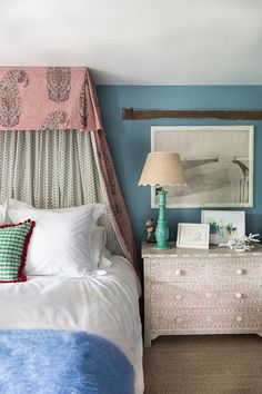 a bedroom with blue walls and white bedding has a pink canopy over the headboard