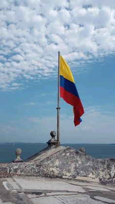 a flag flying on top of a building next to the ocean with clouds in the sky