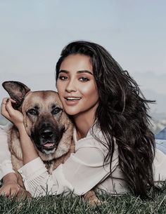 a woman laying in the grass with her dog on her lap and smiling at the camera