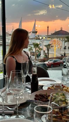 a woman sitting at a table in front of a window with wine glasses on it