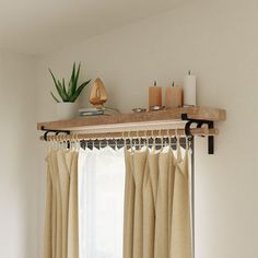 a window with curtains and candles on top of it in front of a white wall