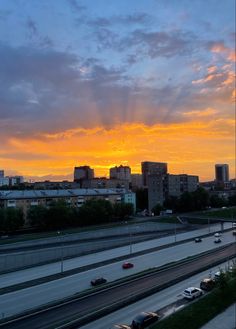 the sun is setting over a city with tall buildings and cars driving down the road