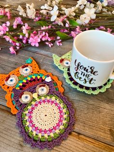 two crocheted coasters sitting on top of a wooden table next to a coffee cup