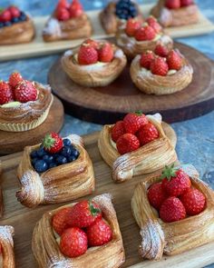 small pastries with strawberries and blueberries are on wooden trays next to each other