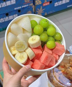 a person holding up a bowl of fruit with grapes, watermelon and bananas