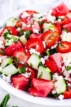 a salad with strawberries, cucumbers and feta cheese on top in a white bowl