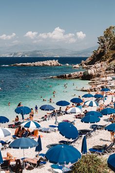 many people are on the beach with blue umbrellas and white sand, while others swim in the water