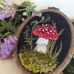 three embroidered mushrooms on black fabric with purple flowers in the foreground and green grass behind them