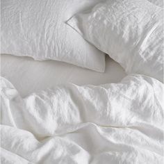 an unmade bed with white sheets and pillows