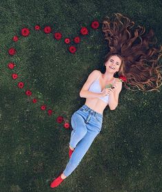 a woman laying in the grass with her hair blowing in the wind and flowers scattered around her