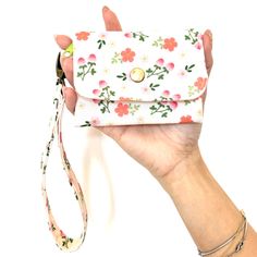 a hand holding a white purse with pink flowers on it and a lanyard strap