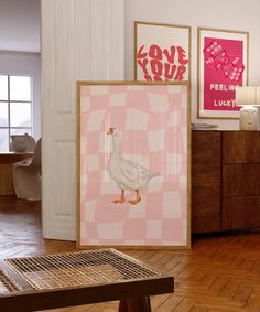 there is a white duck standing in front of two pink pictures on the wall,