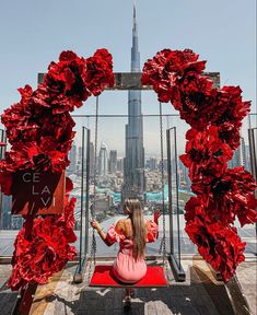 a woman sitting on top of a building in front of a red flowered arch