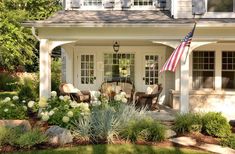 an american flag is hanging on the front door of a white house with flowers and shrubs