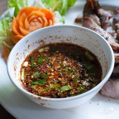 a white plate topped with meat and vegetables next to a bowl of sauce on top of it